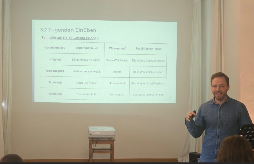 Jakob Steiniger hält einen Vortrag über die Tugenden mit einer Powerpoint Präsentation im Hintergrund